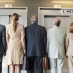 Five businesspeople in suits stand with their backs to the camera, waiting at two elevator doors; LEO LIFT logo visible above.