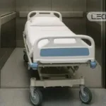 Hospital patient bed on a wheeled transport trolley inside an elevator, ready for patient transfer.