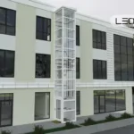 Modern three-story building with a glass-enclosed external elevator shaft in the center.