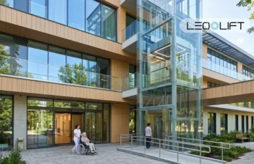 Modern glass-fronted building with an external glass elevator; a caregiver pushes an elderly person in a wheelchair at the entrance; Leo Lift logo.