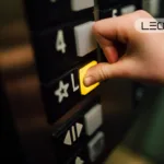 Close-up of a hand pressing a yellow elevator call button on a dark control panel