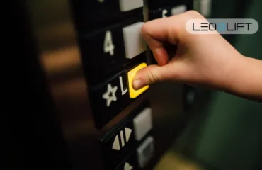 Close-up of a hand pressing a yellow elevator call button on a dark control panel